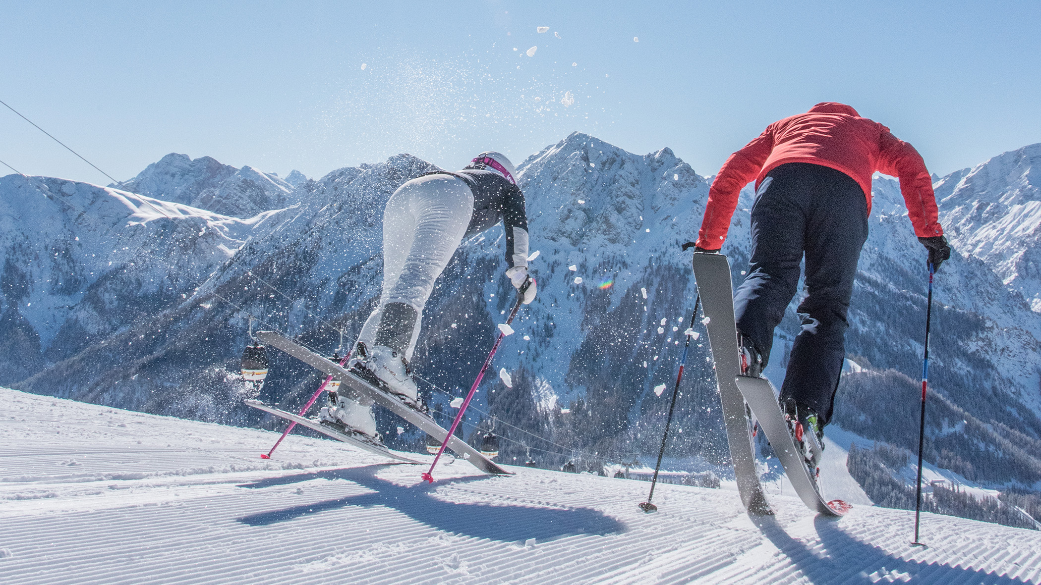 Zwei Skifahrer lassen sich einen verschneiten Berghang hinuntergleiten, im Hintergrund ragen hohe, schneebedeckte Gipfel empor. - Mirabell Dolomites Hotel