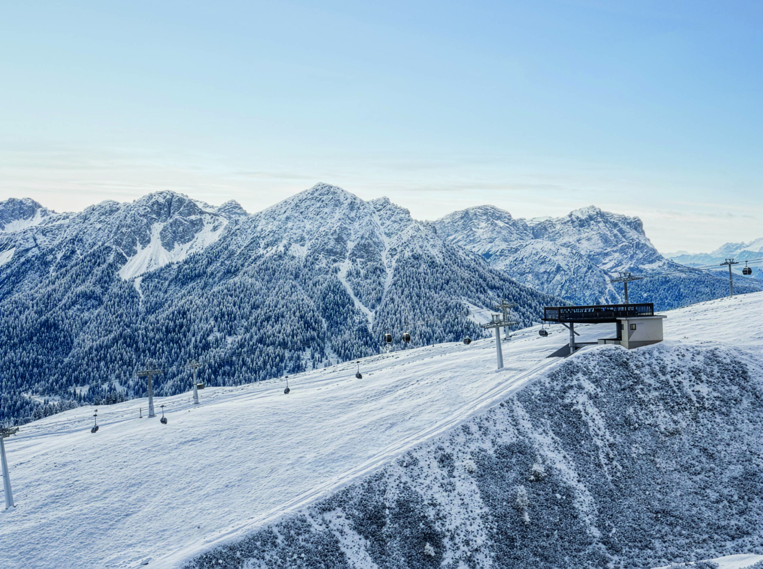 Verschneite Bergkette mit Skilift und blauem Himmel im Hintergrund. - Mirabell Dolomites Hotel