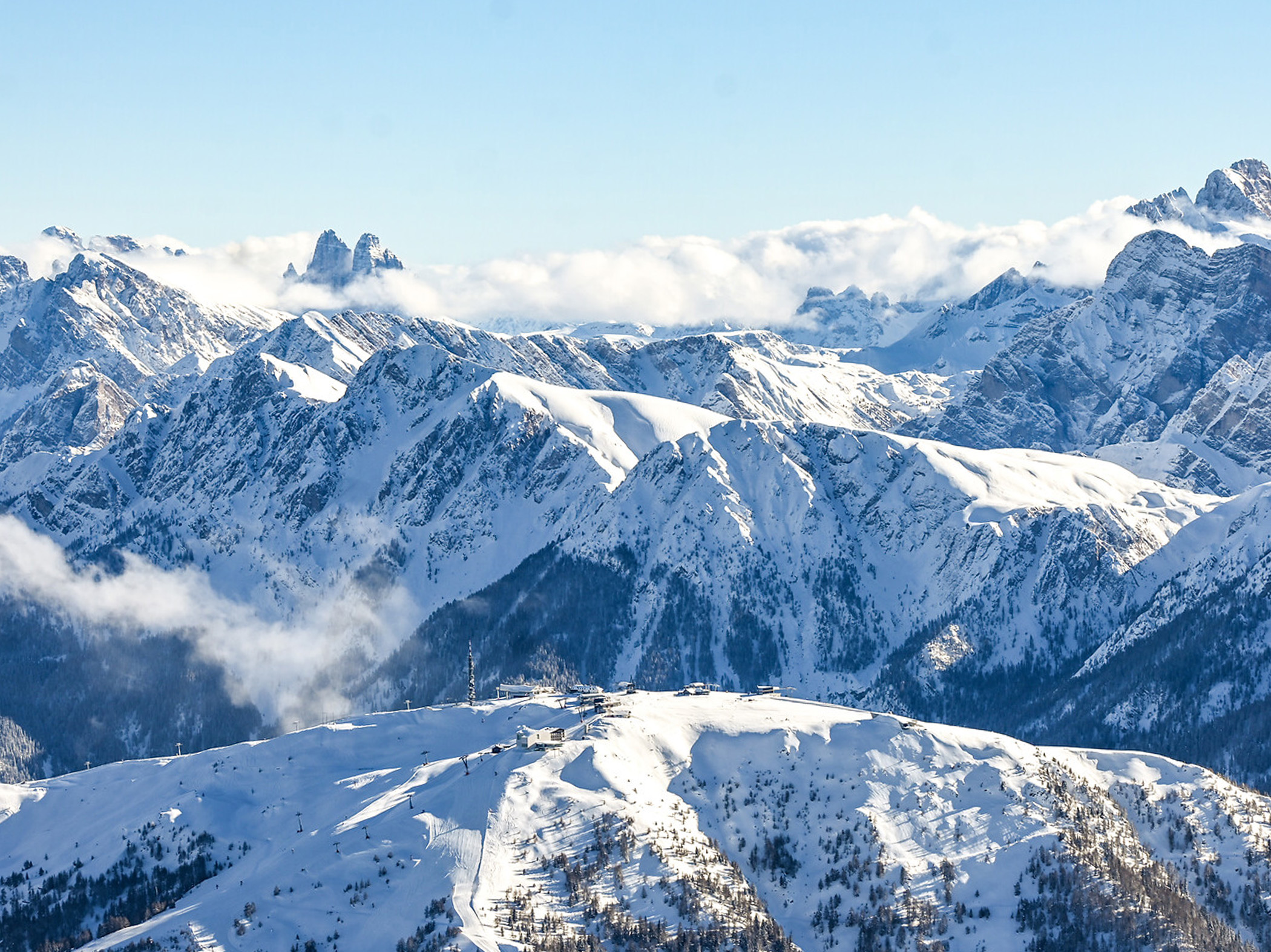 Schneebedeckte Berge unter einem strahlend blauen Himmel, zwischen den Gipfeln ziehen Wolken dahin. - Mirabell Dolomites Hotel