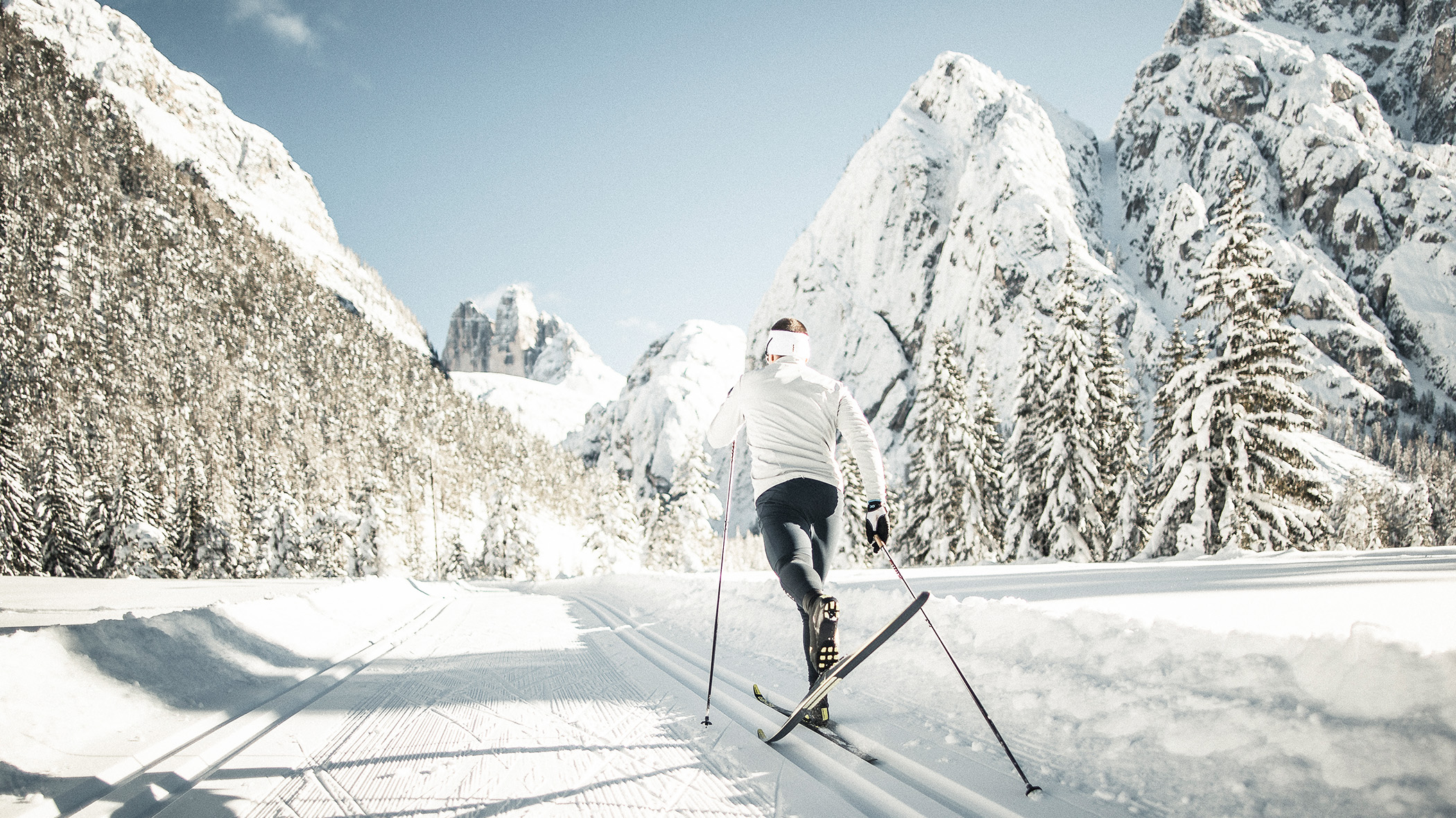 Eine Person, die auf einer verschneiten Loipe Langlauf betreibt, im Hintergrund hohe, schneebedeckte Berge. - Mirabell Dolomites Hotel