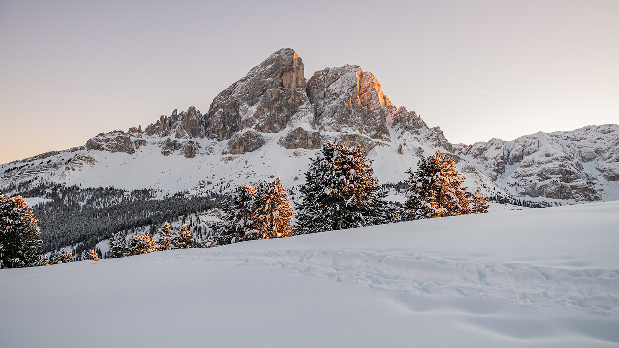 Verschneite Berglandschaft mit sonnenbeschienenen Kiefern und klarem Himmel bei Sonnenaufgang oder Sonnenuntergang. - Mirabell Dolomites Hotel